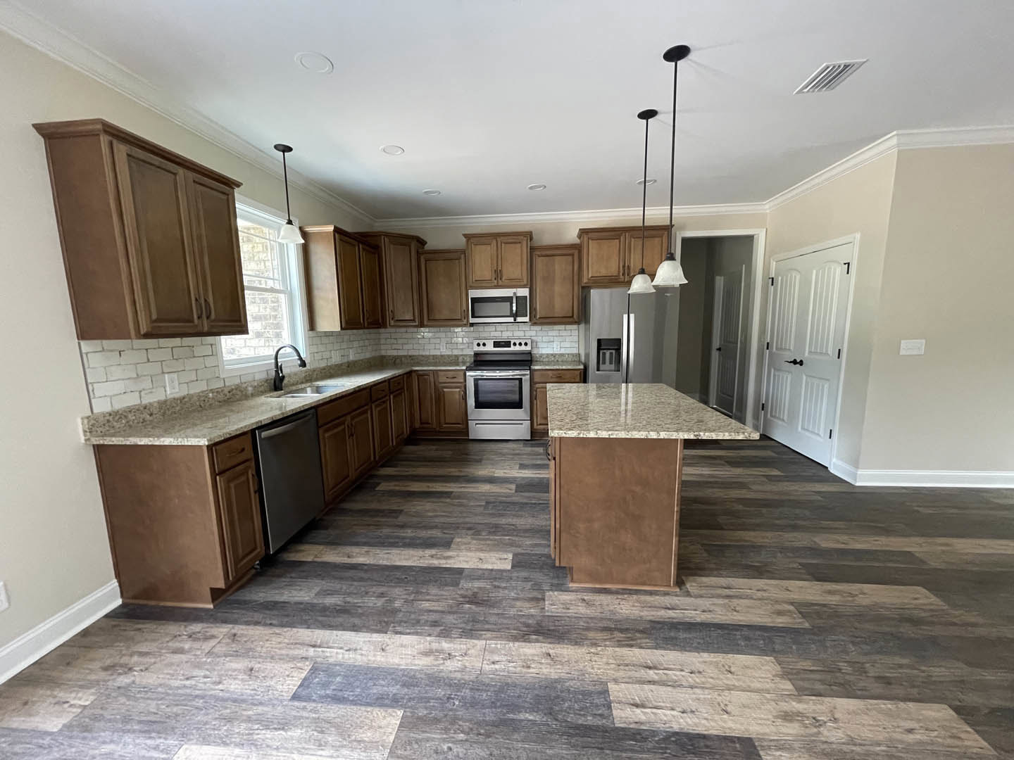 Kitchen with wood flooring, white cabinetry, stainless steel stove and microwave, black hardware, white door, modern faucet, and dark framed appliance.
