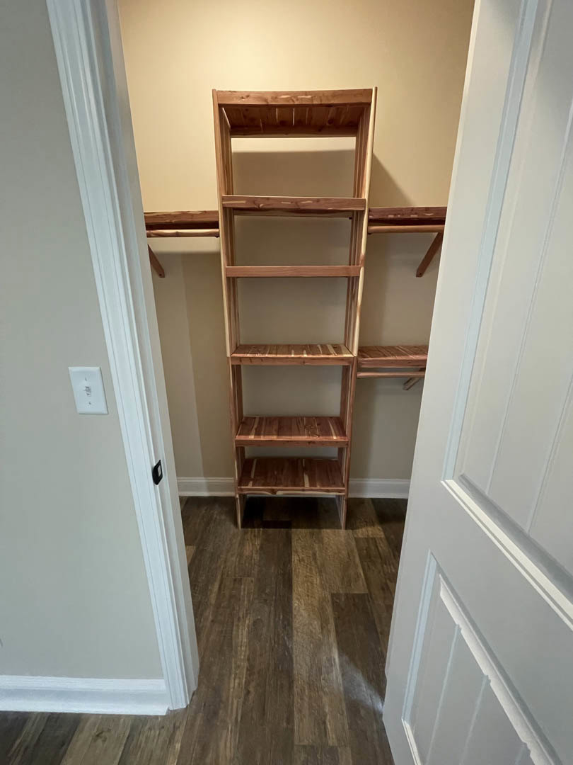 Walk-in closet with built-in wooden shelves, white walls, wood flooring, white baseboard trim, and visible electrical outlet and light switch