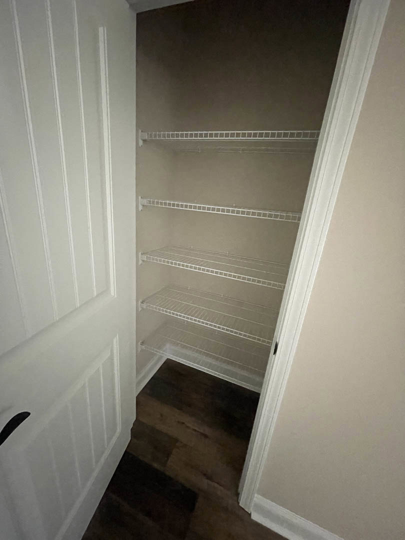 Walk-in closet with built-in white shelves, dark wood flooring, white trim, and a white ladder leaning against a gray wall.