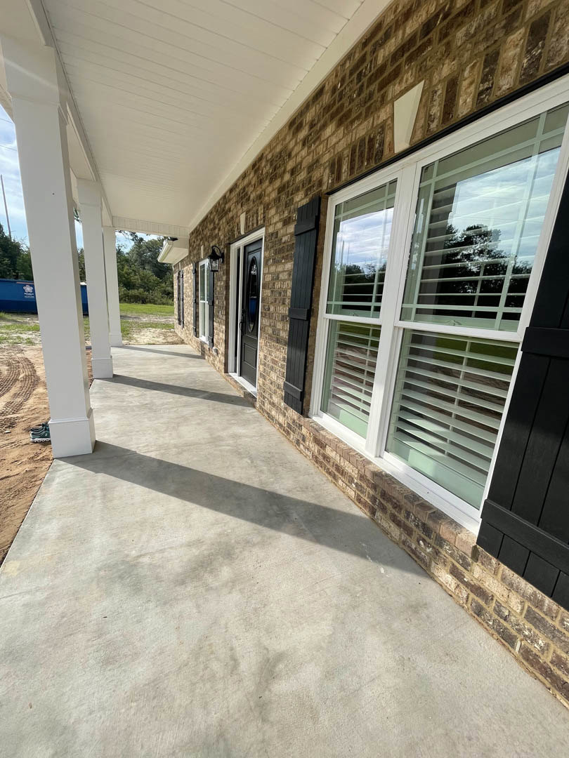 Red brick house with white pillars, covered porch, black shutters, concrete walkway, and window with blinds