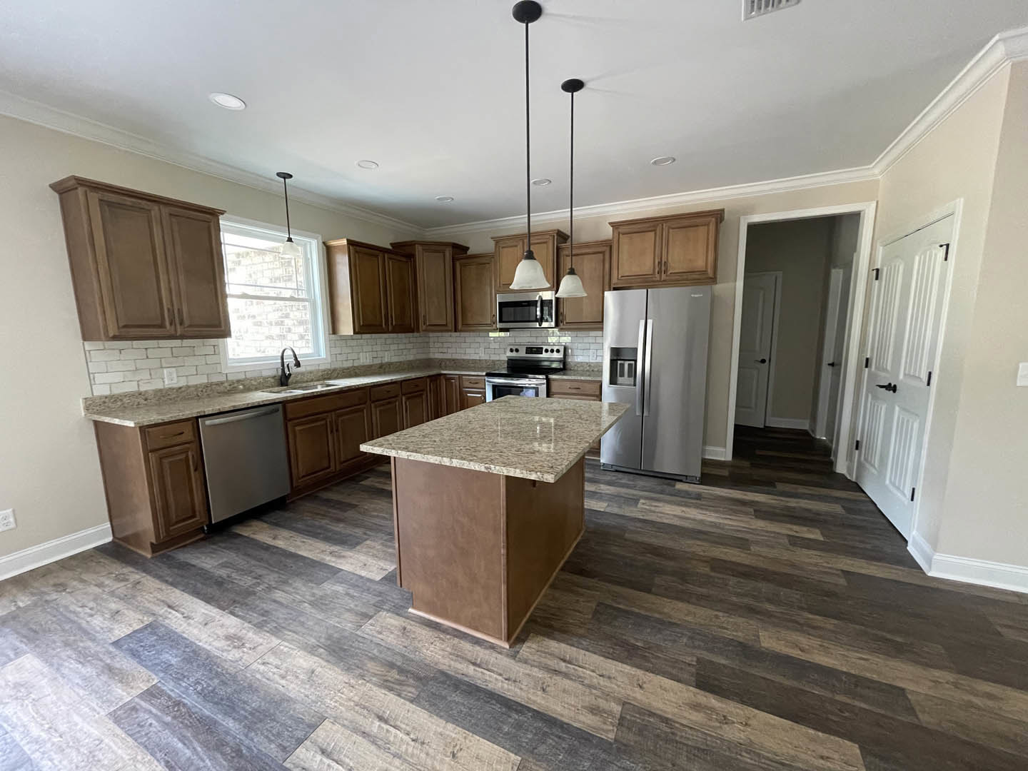 Kitchen with marble-topped island, stainless steel refrigerator, black-door microwave, white cabinetry, black hardware, and built-in dishwasher
