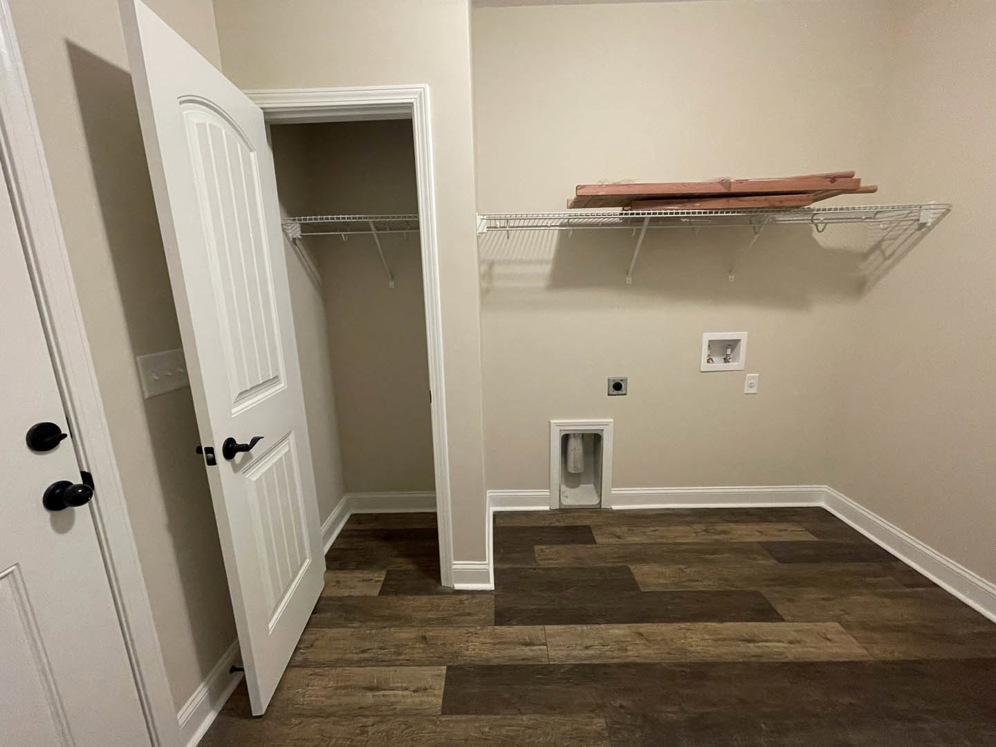 Walk-in closet with light wood flooring, white shelving unit, black door handle, and a recessed metal cylinder in the wall.