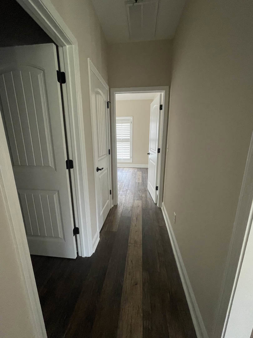 Hallway with white paneled doors, black handles, dark wood laminate flooring, white plaster walls, and a window letting in natural light