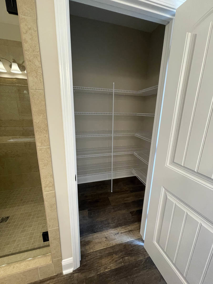 Walk-in closet with built-in white shelves, white paneled walls, white baseboards, and a white door adjacent to a bathroom shower enclosure