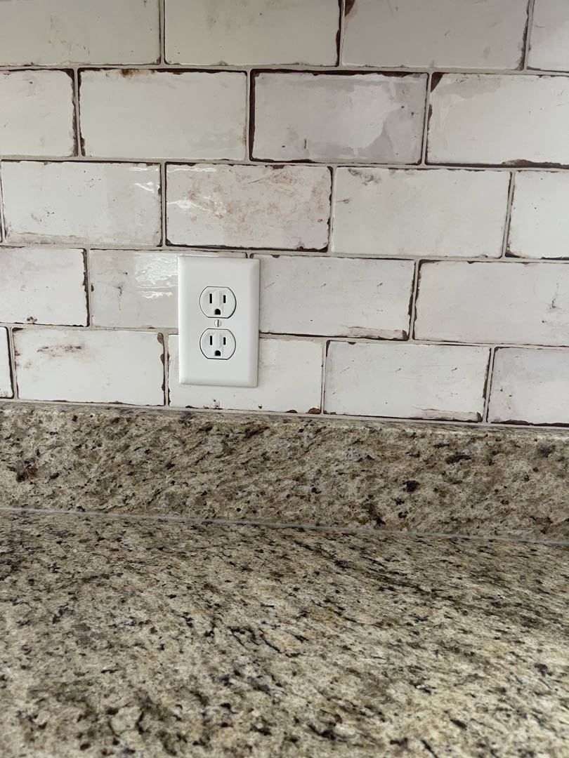 White electrical outlet mounted on glossy white tile backsplash above a countertop