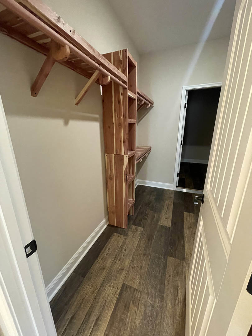 Built-in wooden shelves mounted on a wall above light wood flooring, adjacent to a door with a black screen, in a modern interior room.