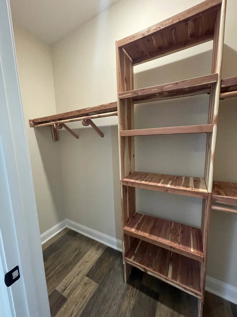 Closet with built-in wooden shelves against a white wall, hardwood flooring visible