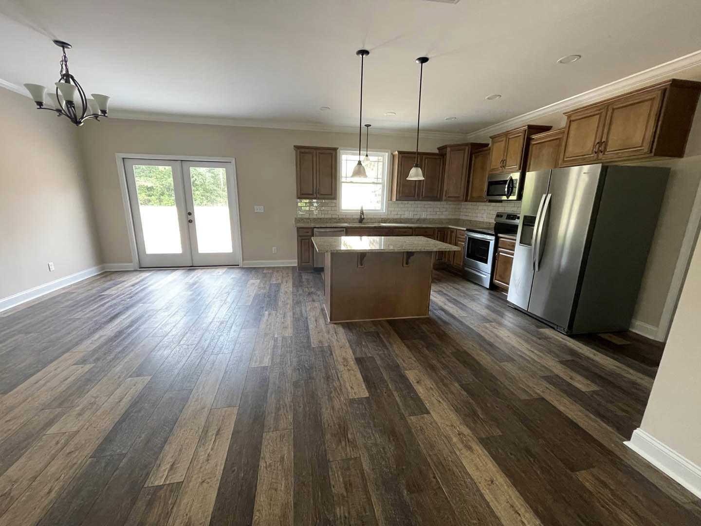 Open kitchen and dining area with hardwood floors, stainless steel refrigerator, glass-paneled double doors, light-colored countertop, built-in microwave, white cabinetry, and