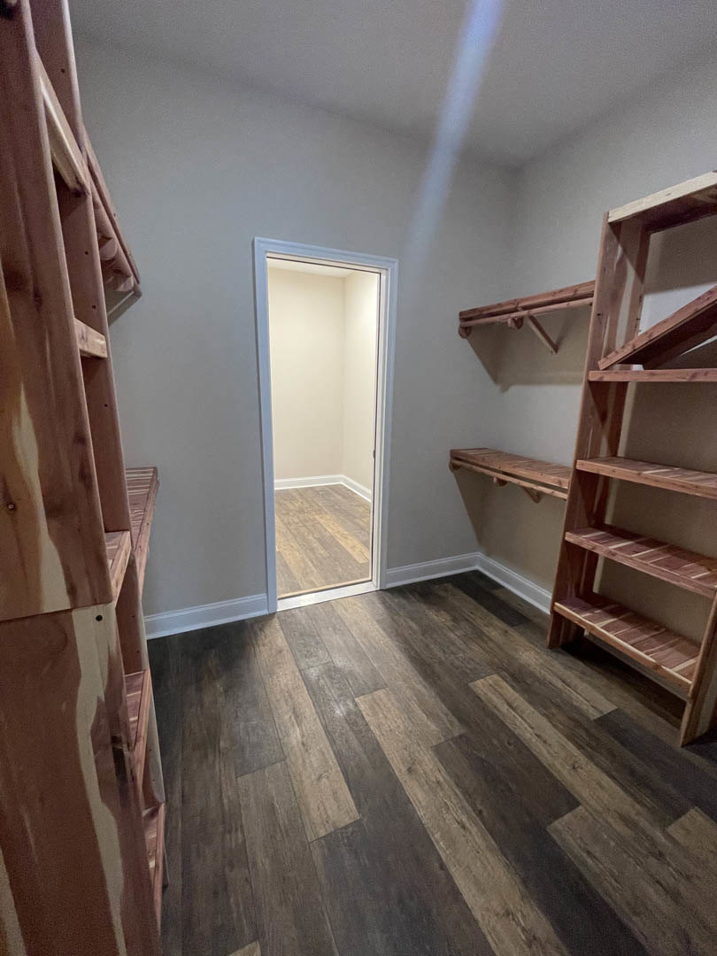 Wood plank flooring, built-in plywood shelves on plaster wall, open door leading to adjacent room