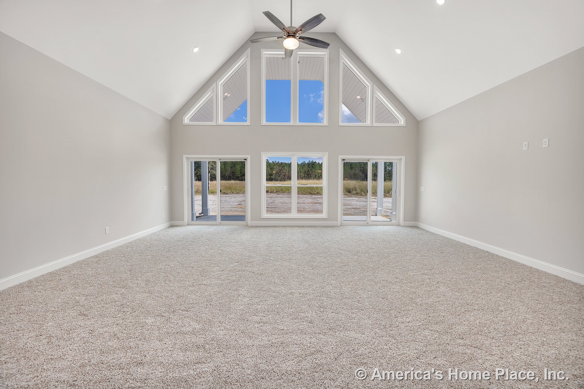 Vaulted ceiling living room with triangular upper windows, sliding glass doors, neutral carpet flooring, recessed lighting, ceiling fan with light, and modern trim details.