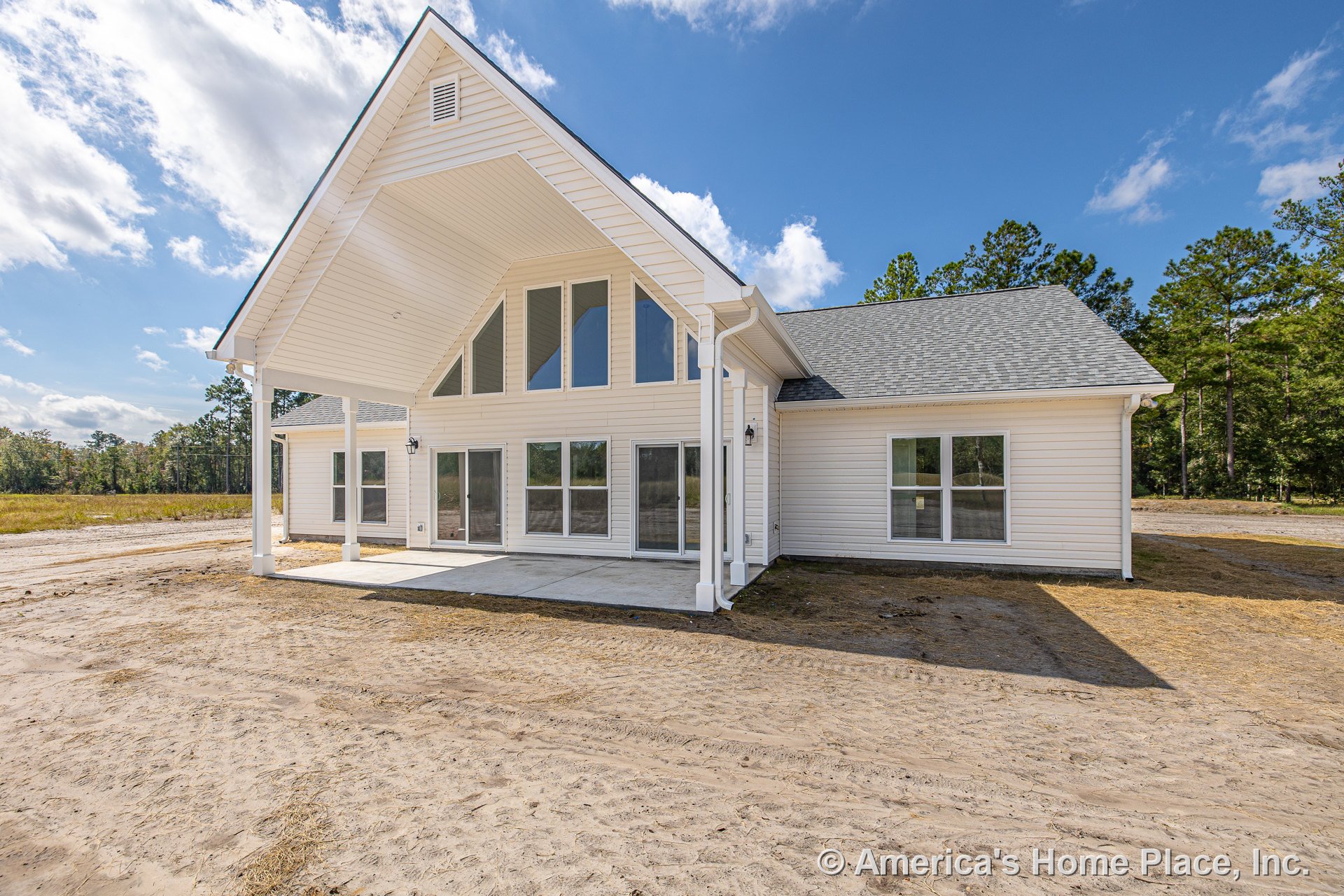 Covered patio with vaulted ceiling, white horizontal siding, multiple large windows, gray shingle roof, concrete patio slab, exterior wall lighting, and porch columns on rear