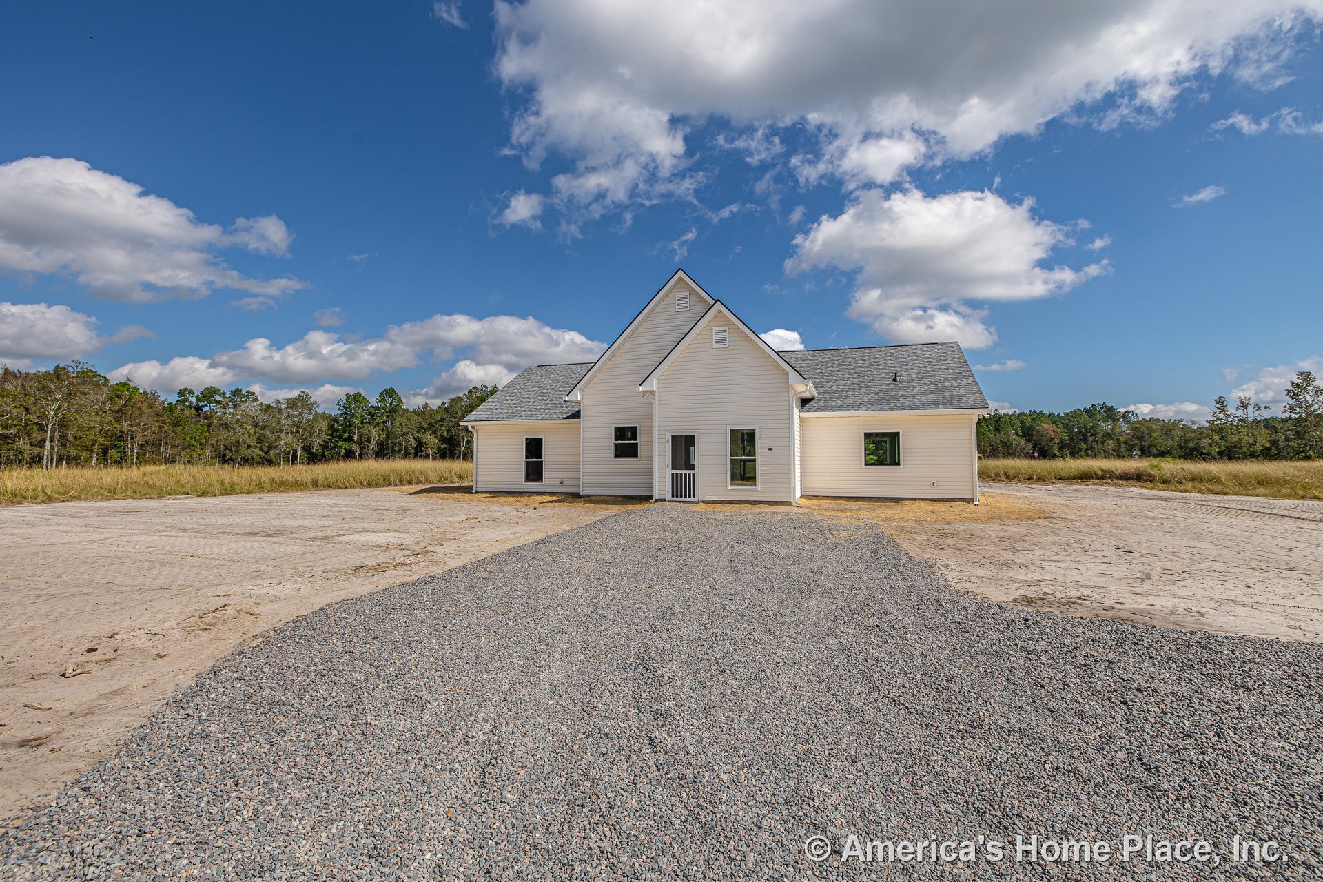 White horizontal siding and gable roof with multiple rectangular windows, covered entry porch, gravel driveway, and rural landscape surrounding single-story new construction.