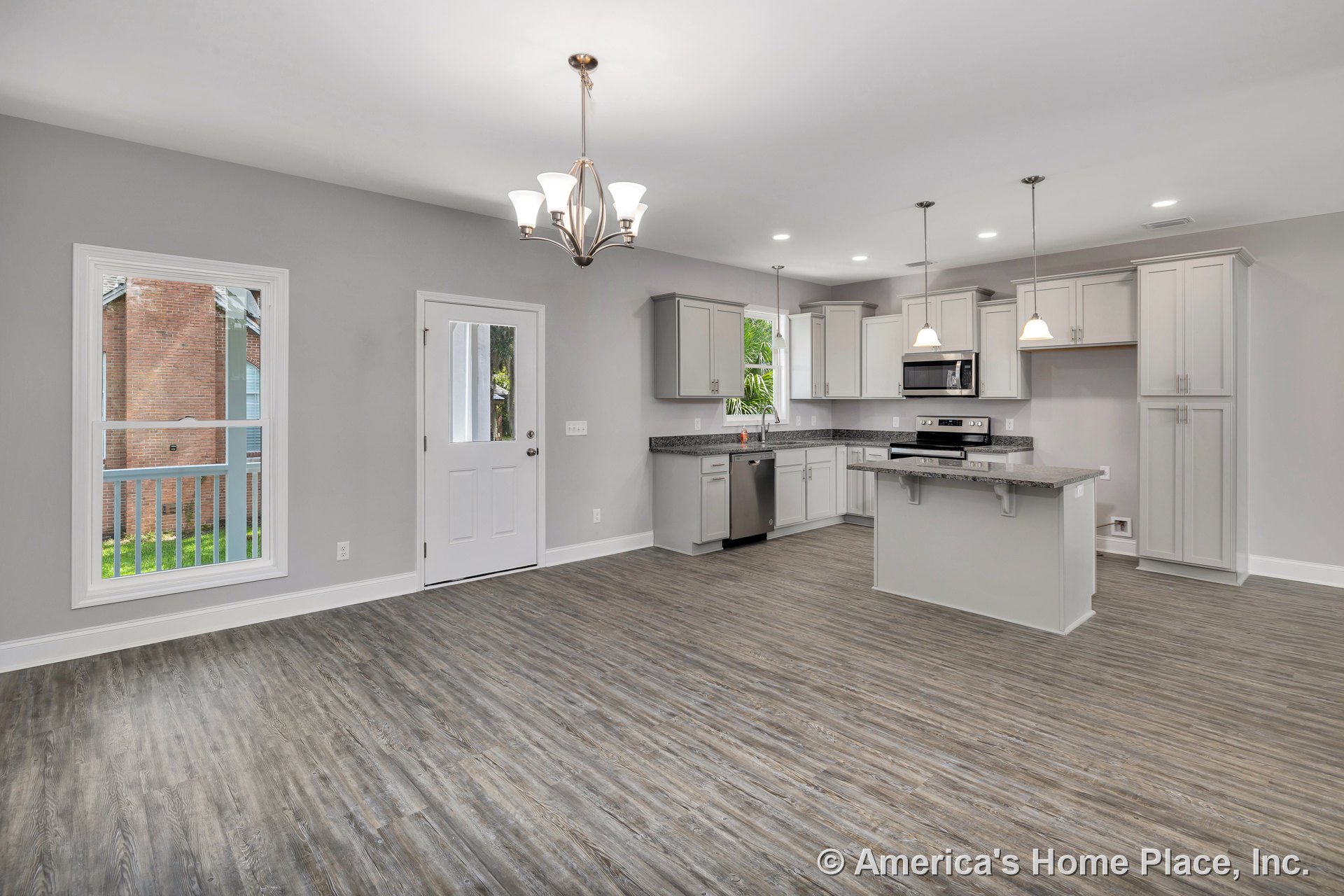 Open kitchen with light gray cabinets, granite countertops, stainless steel appliances, pendant lights above island, wood-look vinyl plank flooring, recessed ceiling lights