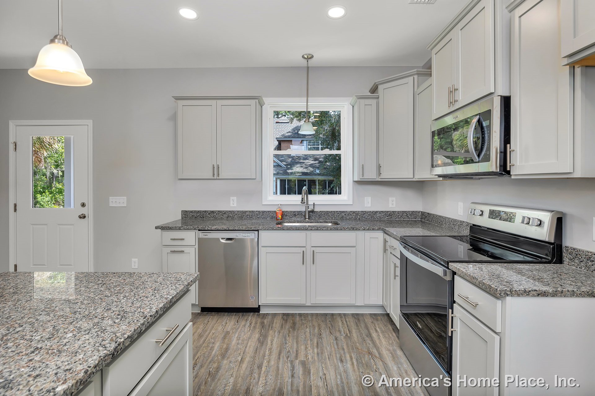 Granite countertops, white shaker-style cabinetry, stainless steel dishwasher and electric range with microwave, single basin sink beneath window, pendant and recessed lighting