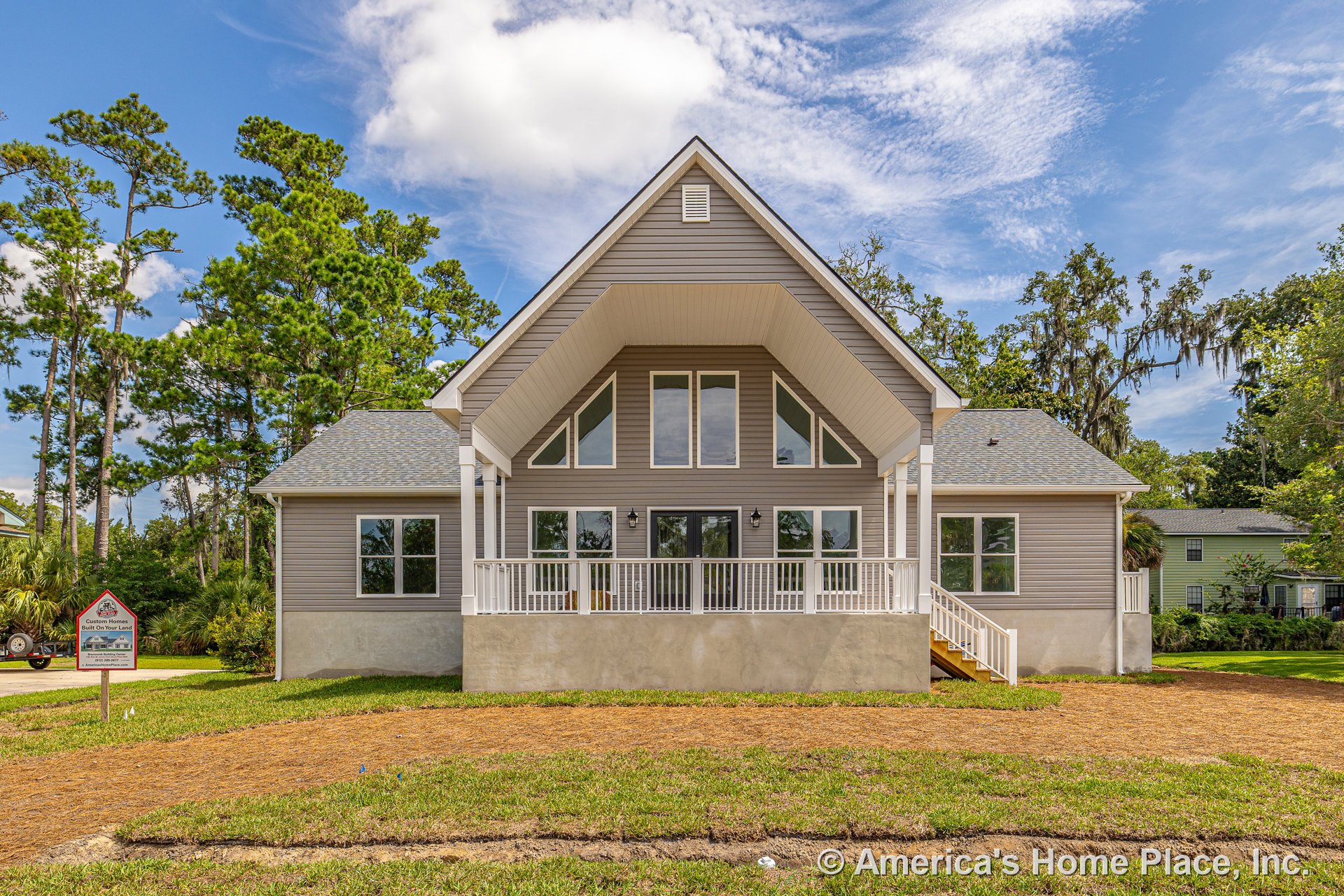Covered front porch with white railing, multiple large windows, gray siding exterior, gabled roof, concrete foundation, entry door, exterior lighting, front stairs, and decorative