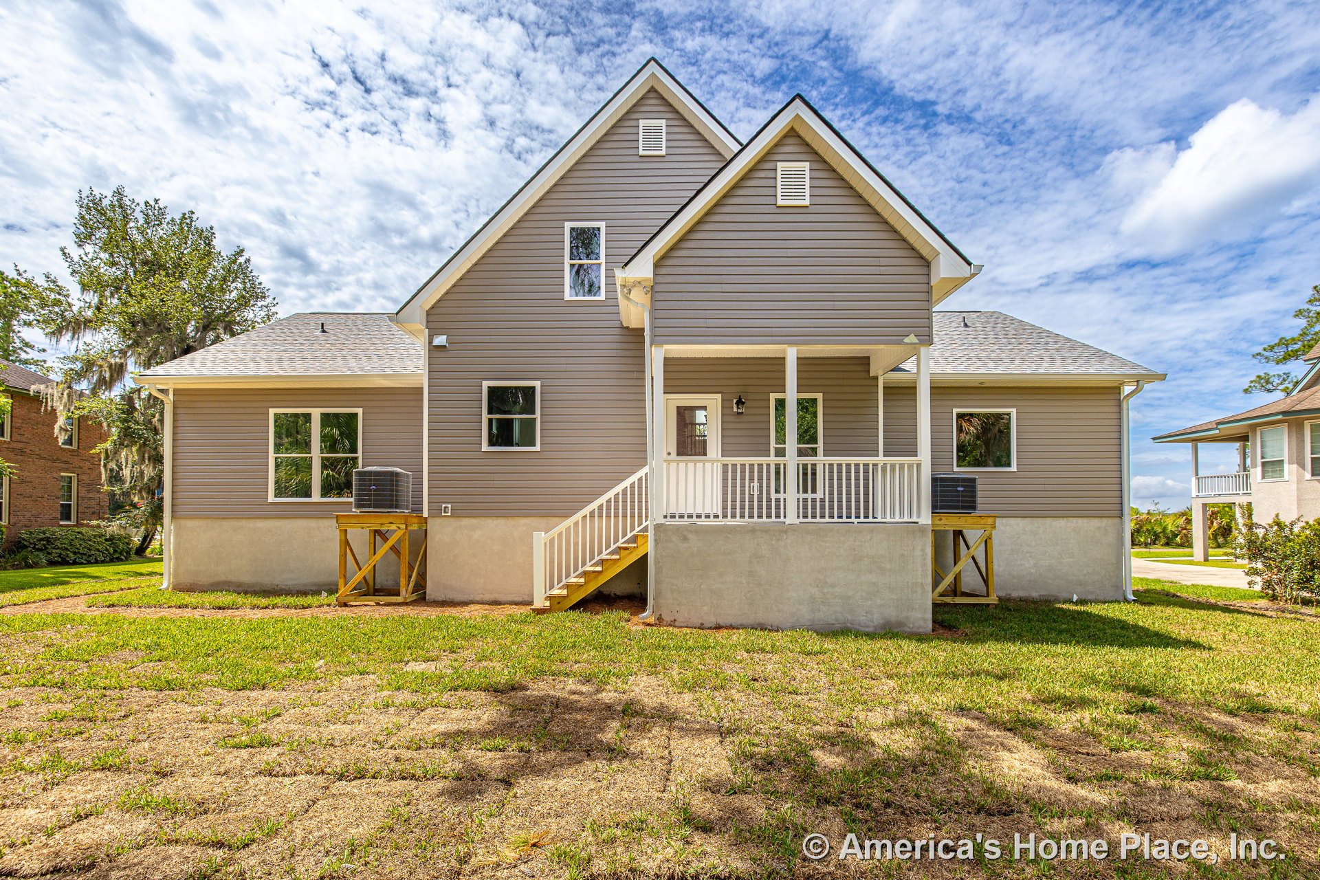 Covered rear porch with white railing and stairs, gray vinyl siding exterior, concrete foundation, multiple rectangular windows, gable roof with vents, built-in porch lighting, and