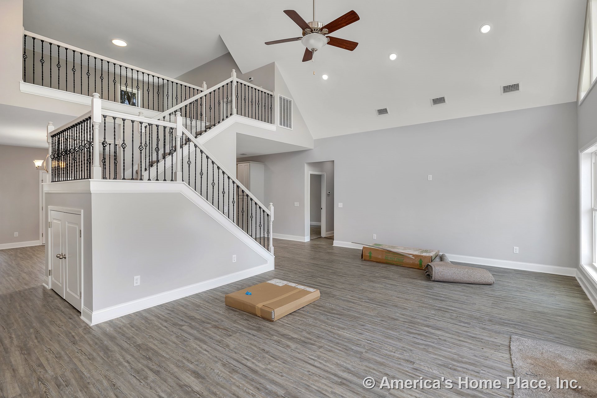 Vaulted ceiling with ceiling fan and recessed lighting, staircase with decorative iron balusters, gray wood-look flooring, large windows, under-stair storage closet, white trim