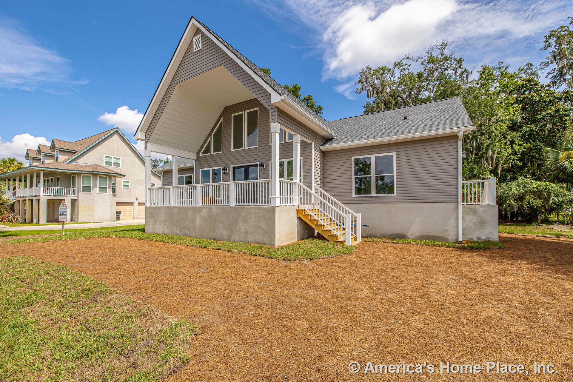 Covered front porch with white railings, gray siding, gable roof, multiple large windows, exterior staircase, and decorative trim.