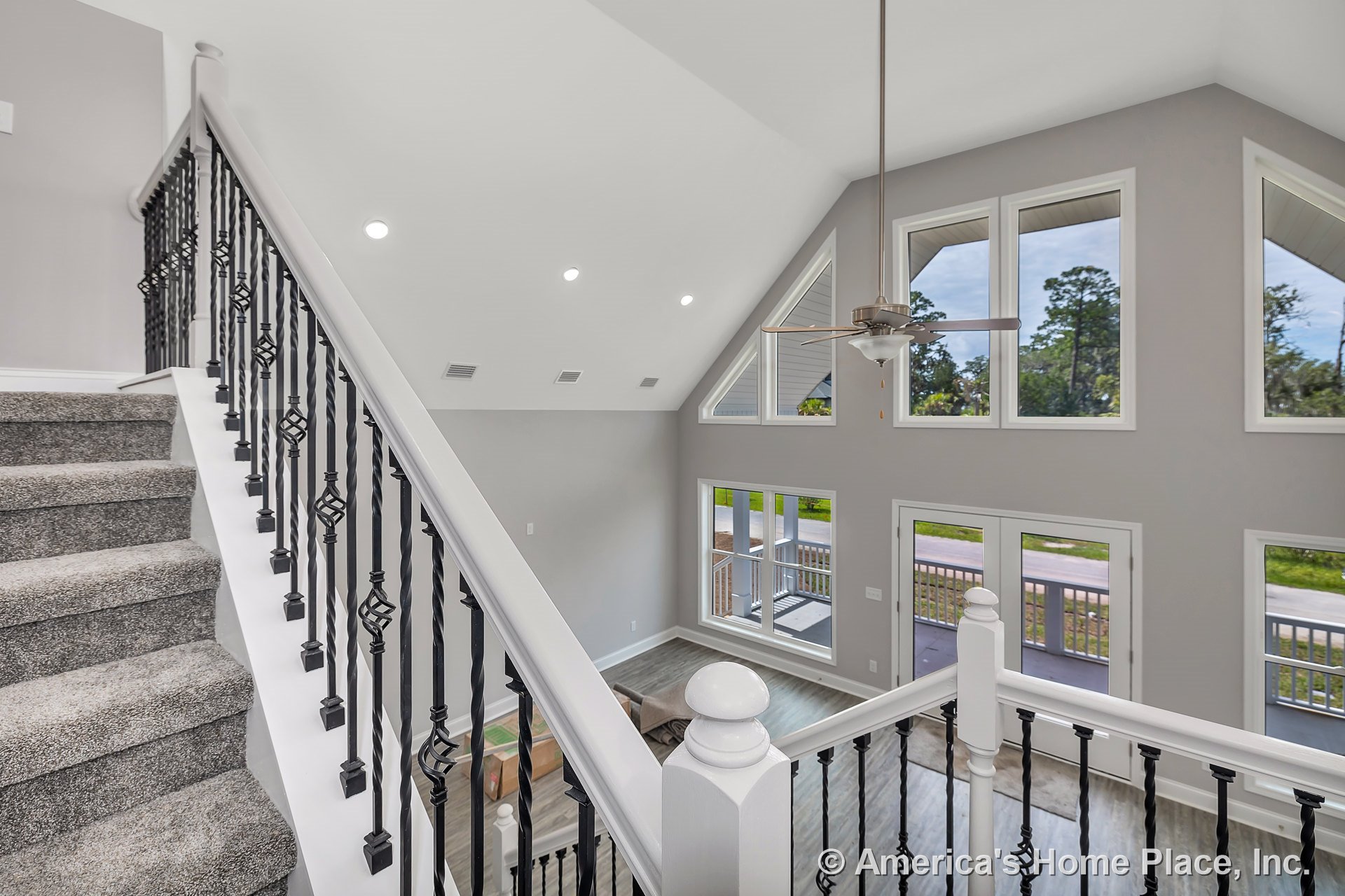 Vaulted ceiling with recessed lighting and ceiling fan, expansive windows framed in white trim, open layout with wood-look flooring, staircase featuring gray carpeted steps and