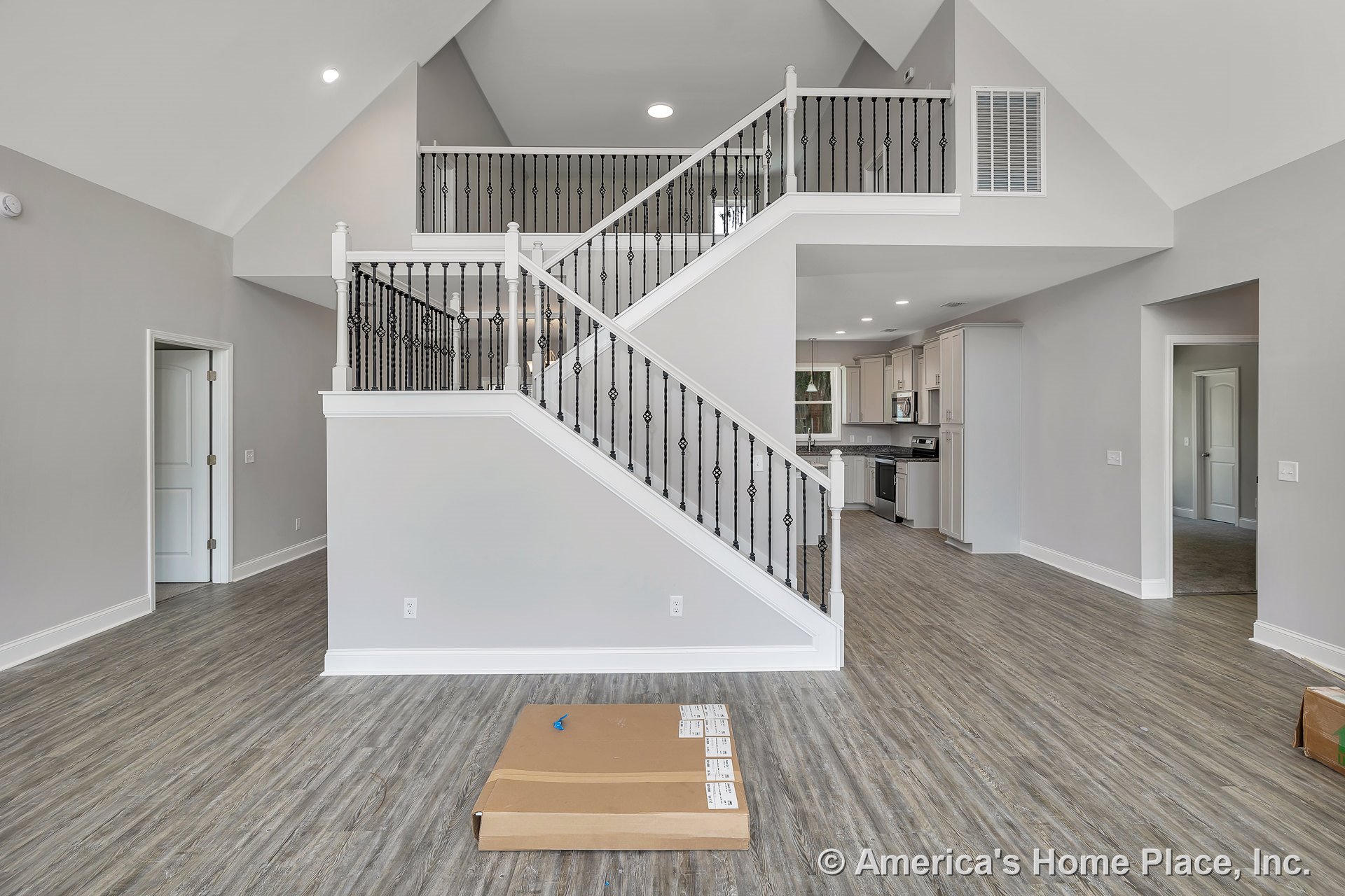 Vaulted ceiling living area with iron stair railings, open entry to kitchen featuring light cabinetry, wood-look flooring, recessed ceiling lights, and white trim with baseboards.