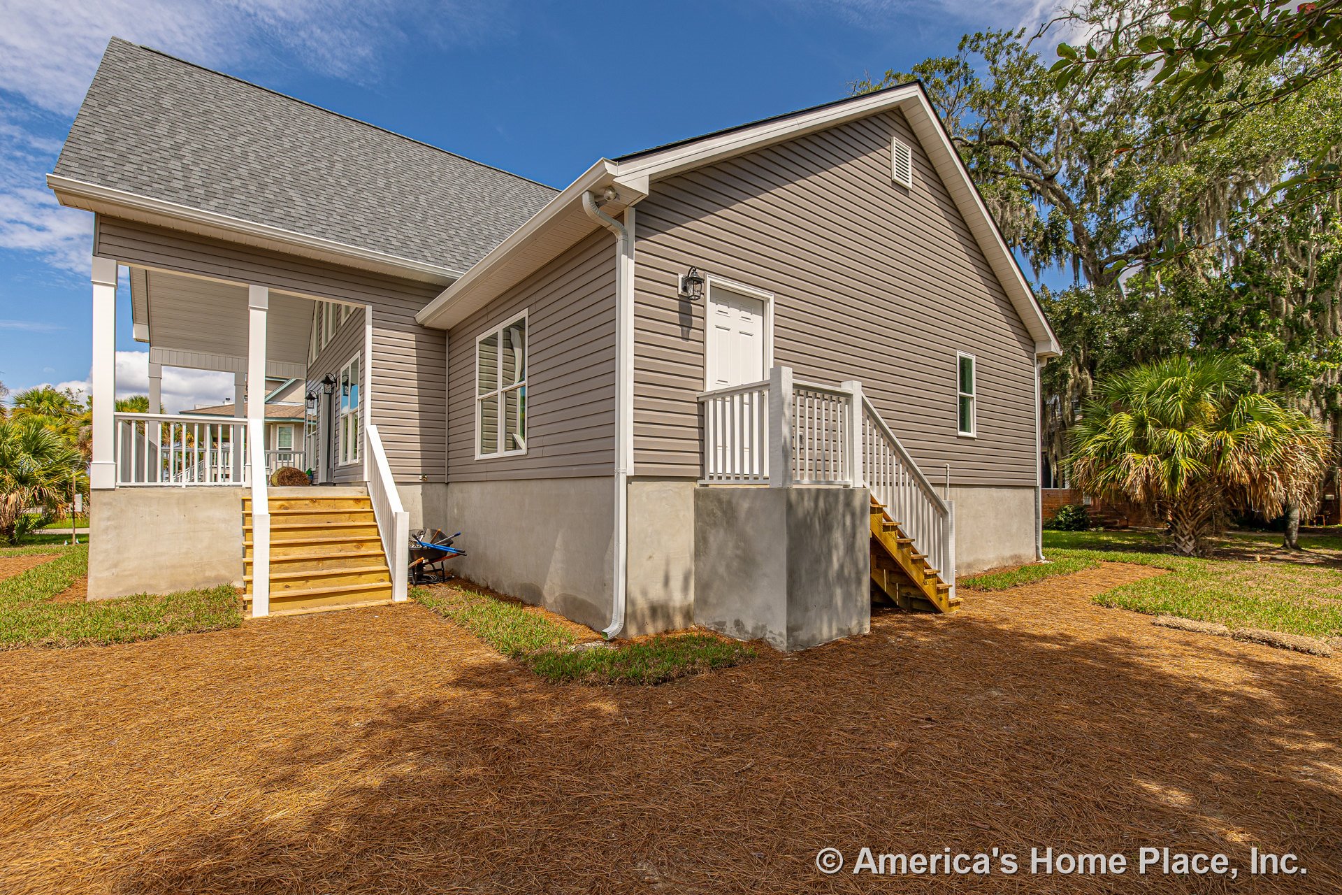 Gray vinyl siding exterior with white trim and railings, covered front porch, double entry doors, multiple windows, two sets of wood stairs, concrete foundation, and outdoor
