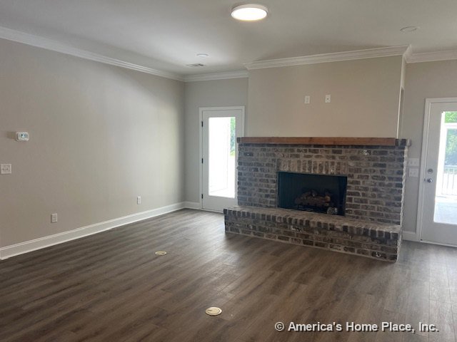 Brick fireplace with wood mantel, vinyl plank flooring, crown molding trim, recessed ceiling light, glass exterior doors, large windows, and neutral wall color in spacious living