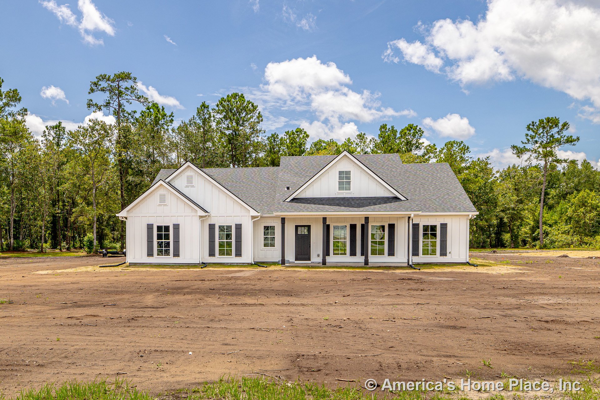 White board-and-batten siding with black shutters, covered front porch, black front door, multiple double-hung windows, gray shingle roof, farmhouse-style trim.