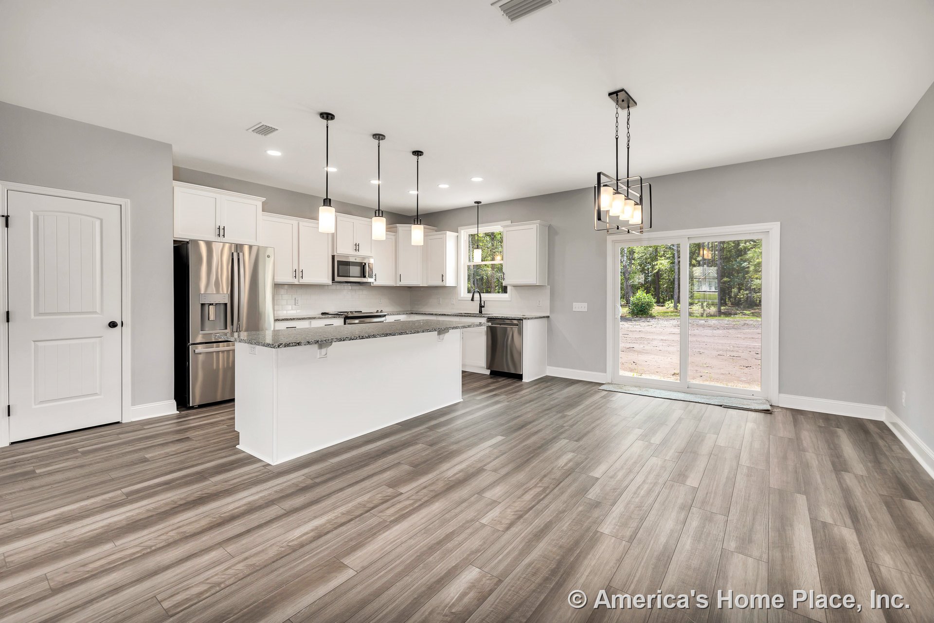 Open concept kitchen and dining area with white shaker cabinets, granite island, stainless steel appliances, pendant and chandelier lighting, wood-look tile floors, and sliding