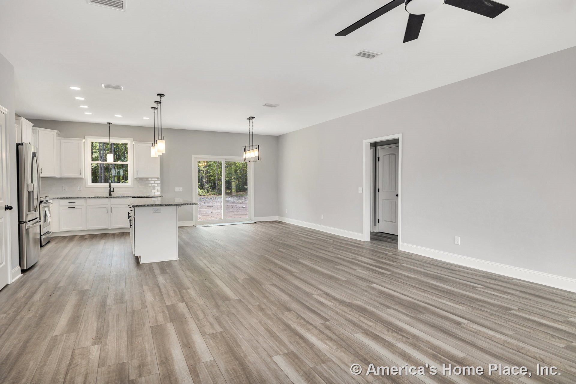 Open-concept kitchen and living area with white shaker cabinets, granite countertops, wood-look vinyl plank flooring, kitchen island, pendant and recessed lighting, sliding glass