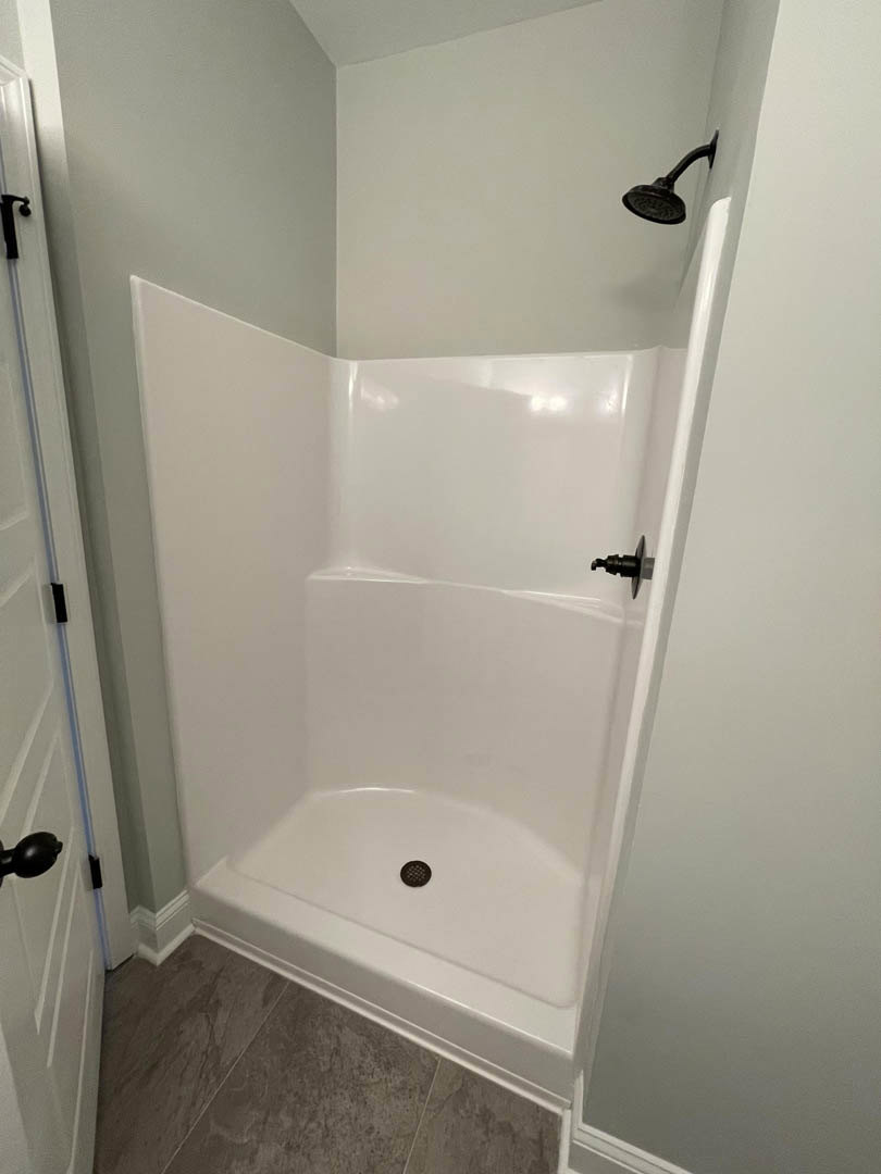 Walk-in shower with white subway tile walls, black metal showerhead and faucet, and light gray tile floor