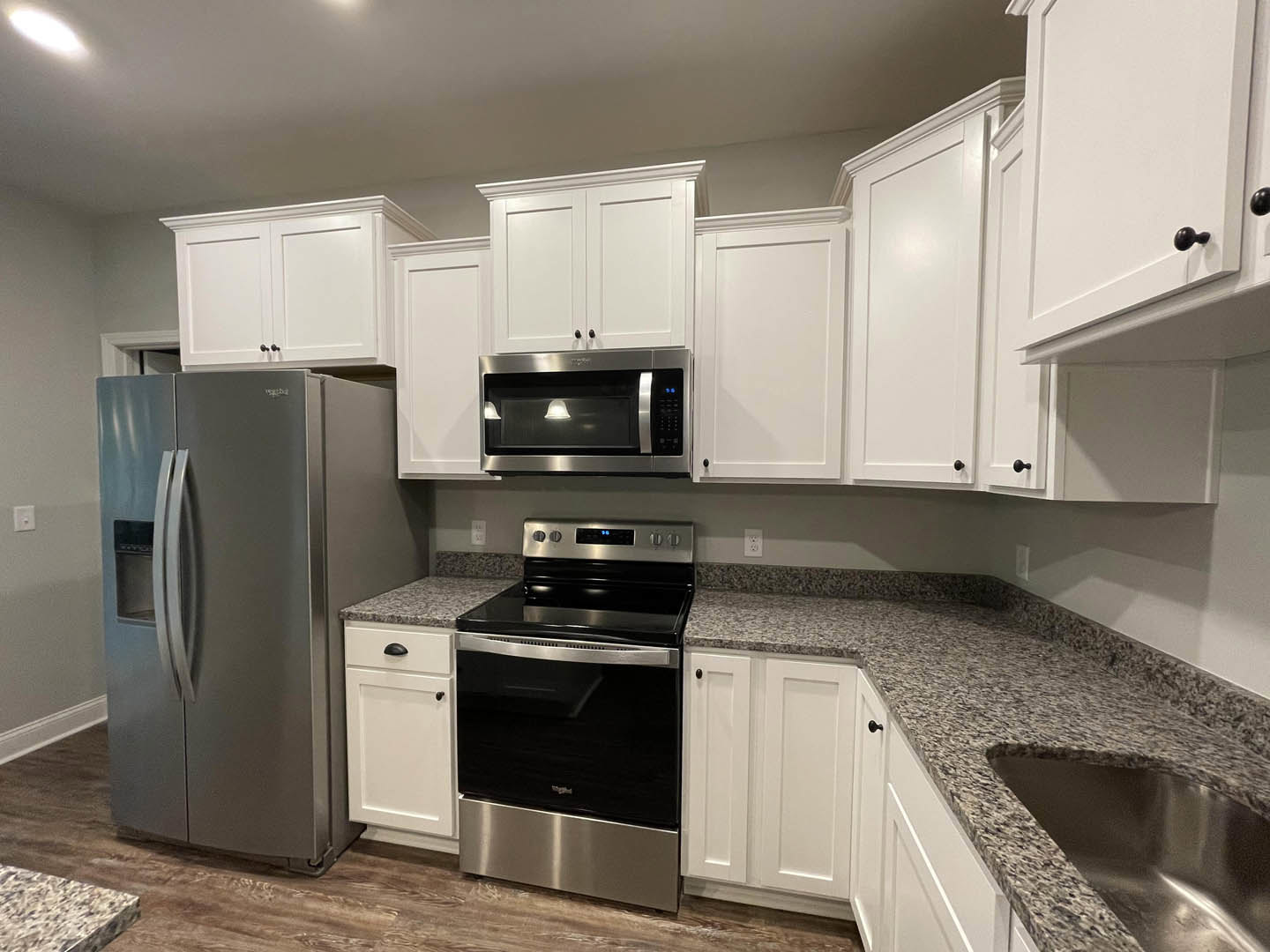 White shaker cabinets, black refrigerator, microwave, and oven, light stone countertops, stainless steel sink, white interior door, neutral walls