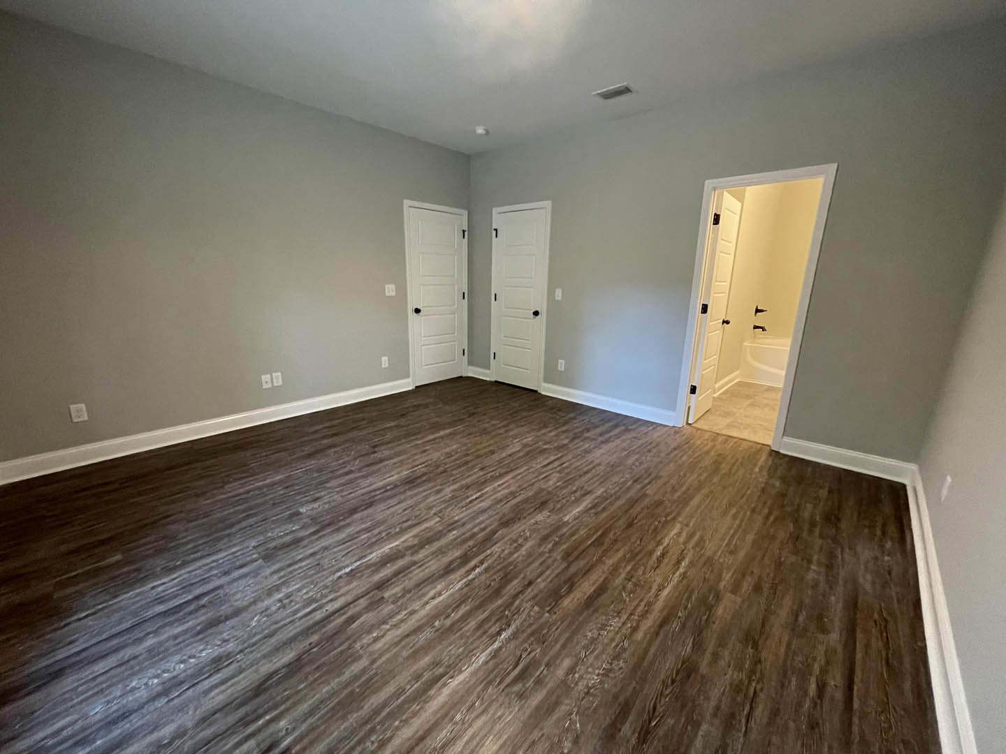 Room with light hardwood flooring, white walls, and multiple white doors featuring black knobs; partial view of a bathroom with a freestanding bathtub through an open doorway.
