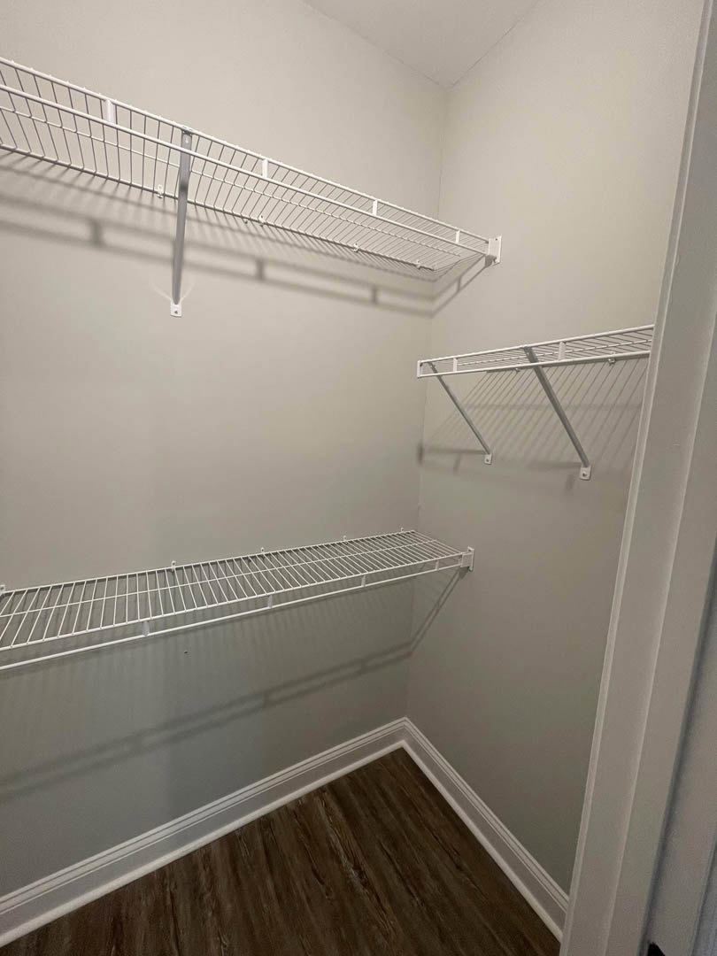 Walk-in closet with white wire shelves mounted on plaster walls, wood flooring, and white ceiling