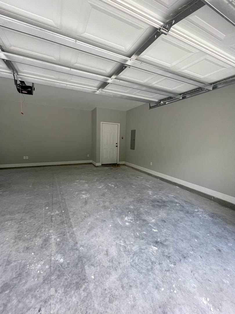 Spacious room with white plaster walls, light flooring, and a large white garage door featuring black hardware