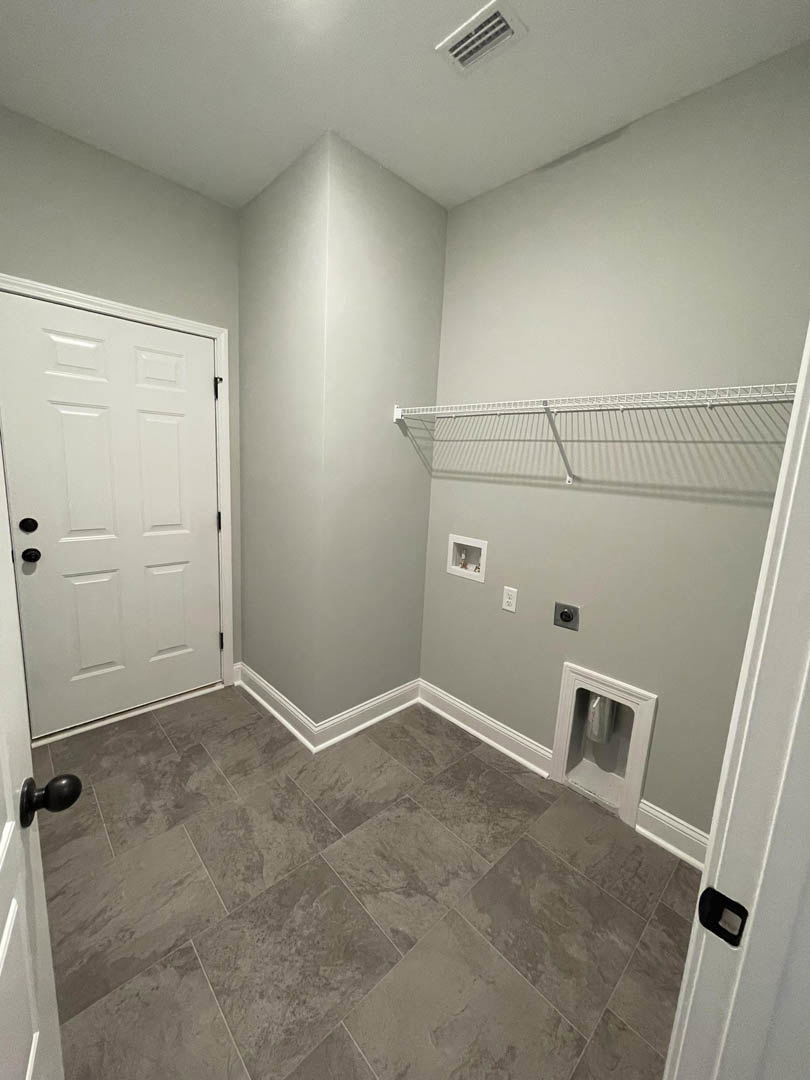 White door with black knobs, white wall and shelf, grey tile floor with white baseboard trim, metal container recessed in wall