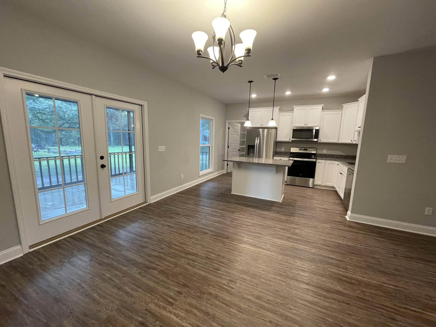 Open kitchen and dining area featuring wood flooring, white cabinetry, stainless steel stove and microwave, glass-paneled double doors, and a modern chandelier above the dining