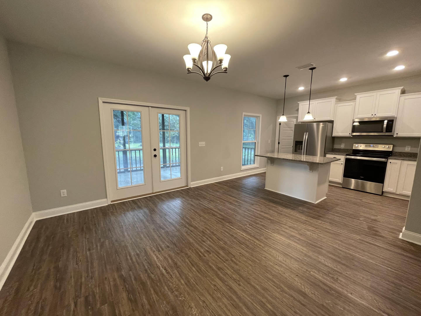 Open kitchen and dining area featuring hardwood floors, white cabinetry, stainless steel stove and microwave, glass-paneled double doors, and a modern chandelier above the dining