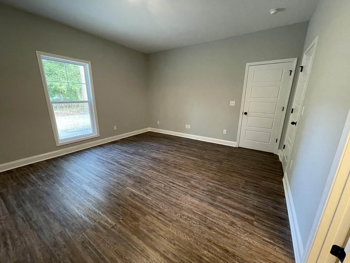 Room with hardwood floor, white walls, white-framed window, white door with black knobs, white ceiling with recessed black light fixture