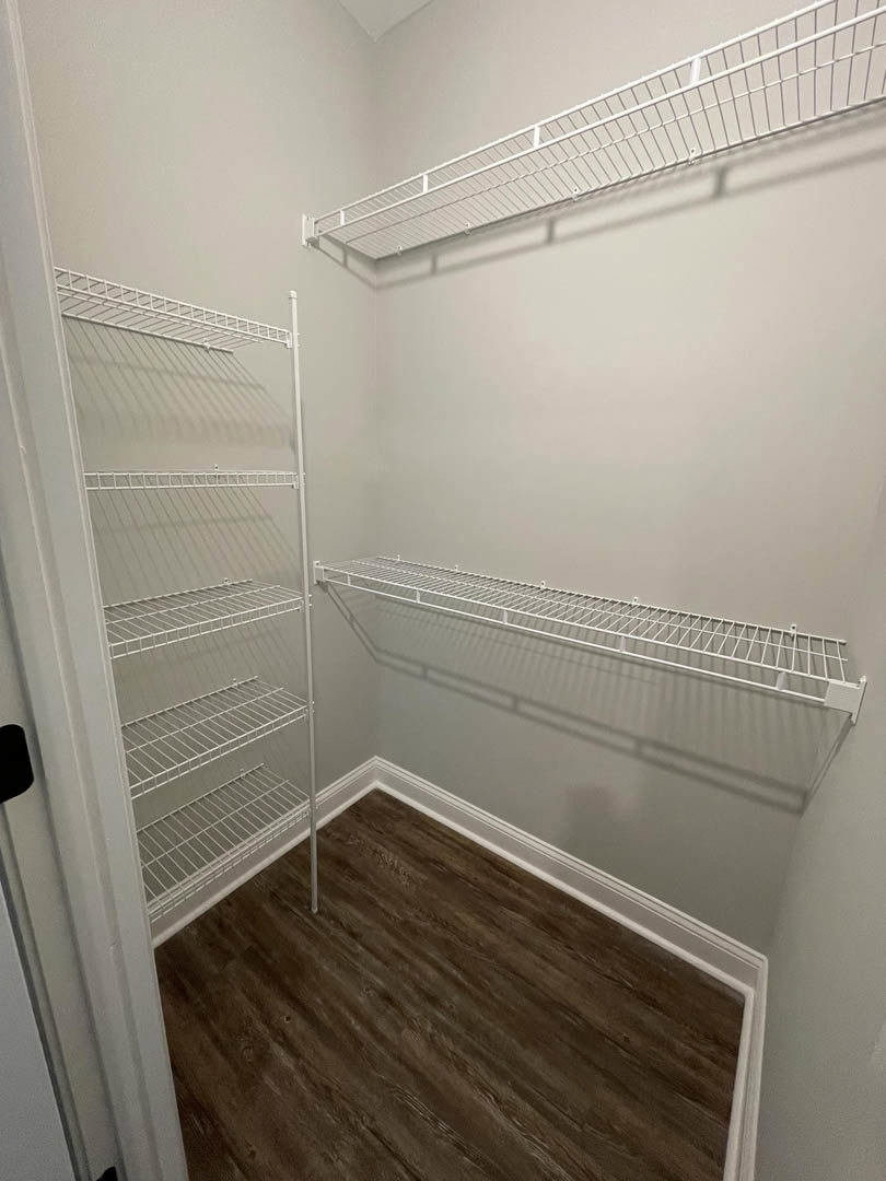 Walk-in closet with white wire shelving, wood plank flooring, white baseboards, and light gray painted walls