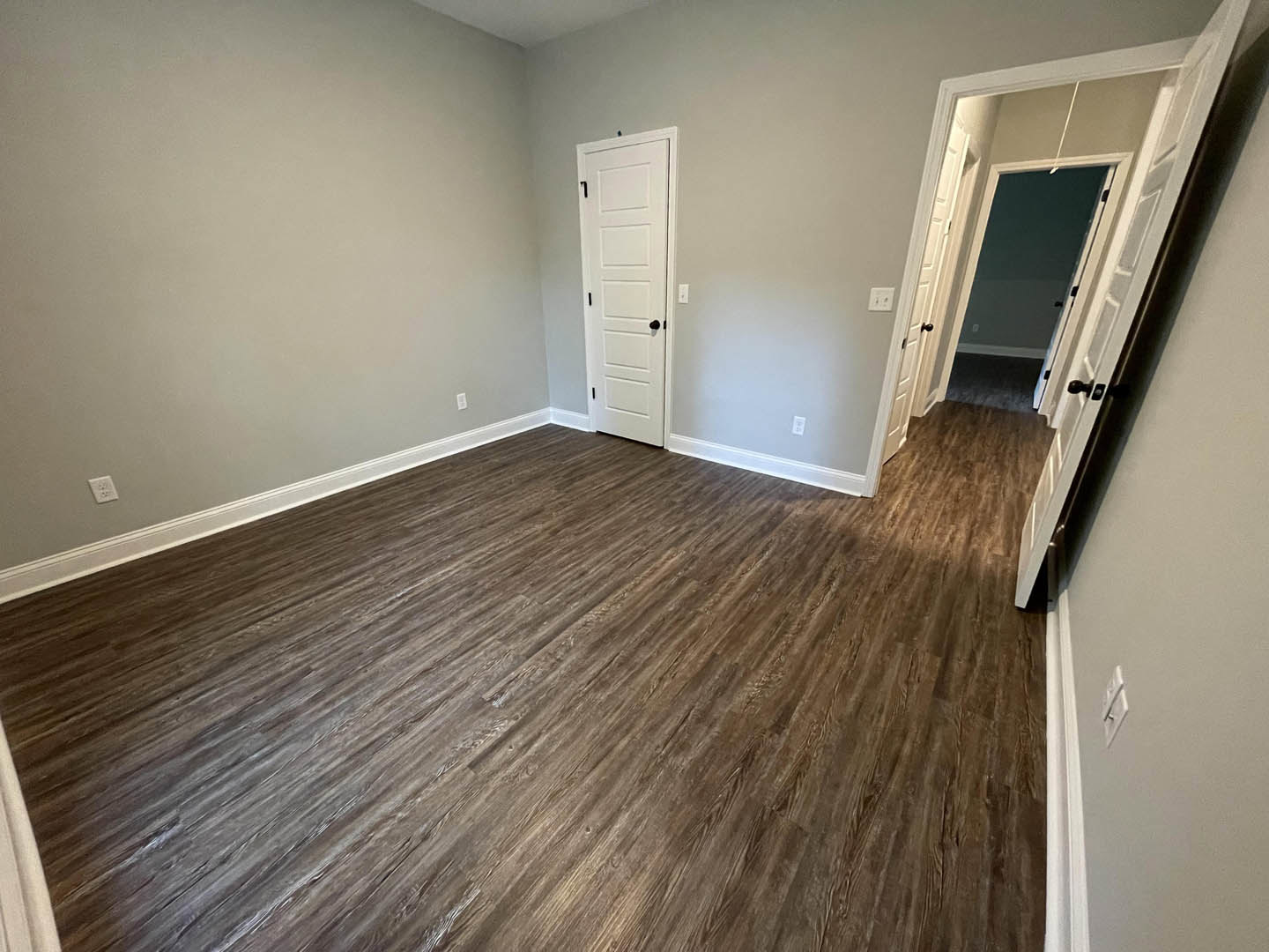 Open doorway leading to a room with hardwood flooring, white walls, and a white door featuring black handles