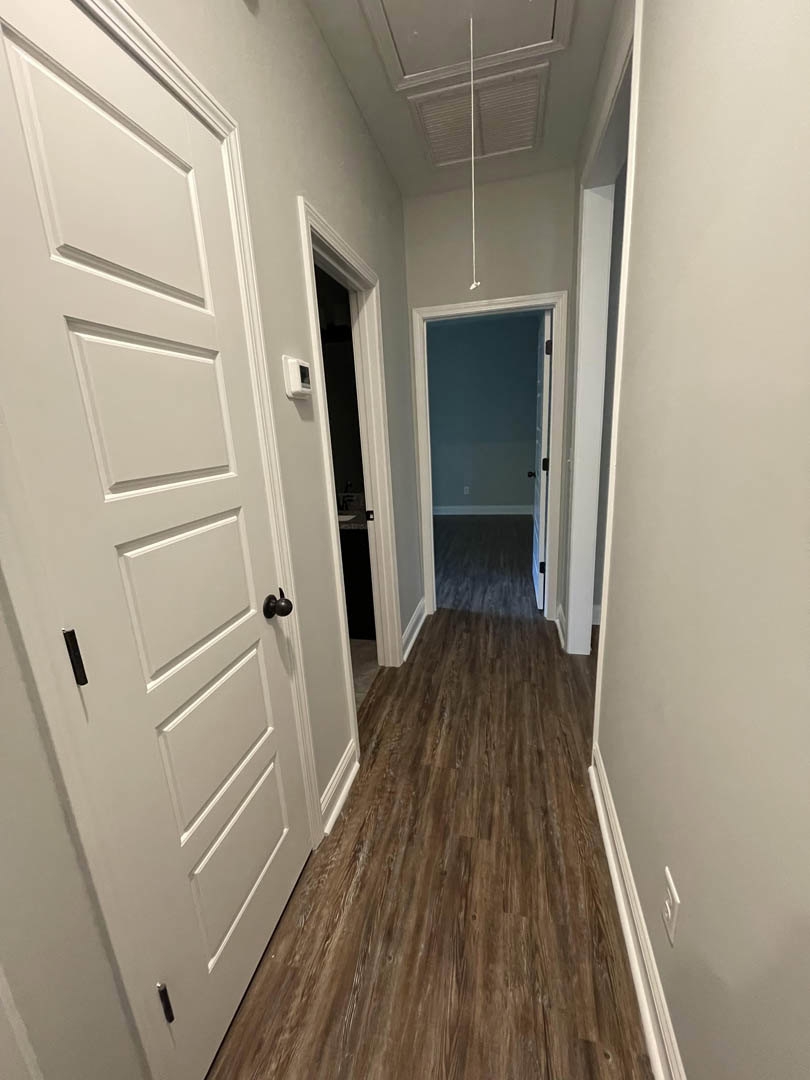 Hallway with light hardwood flooring, multiple white paneled doors featuring black handles, white plaster walls, and smooth white ceiling