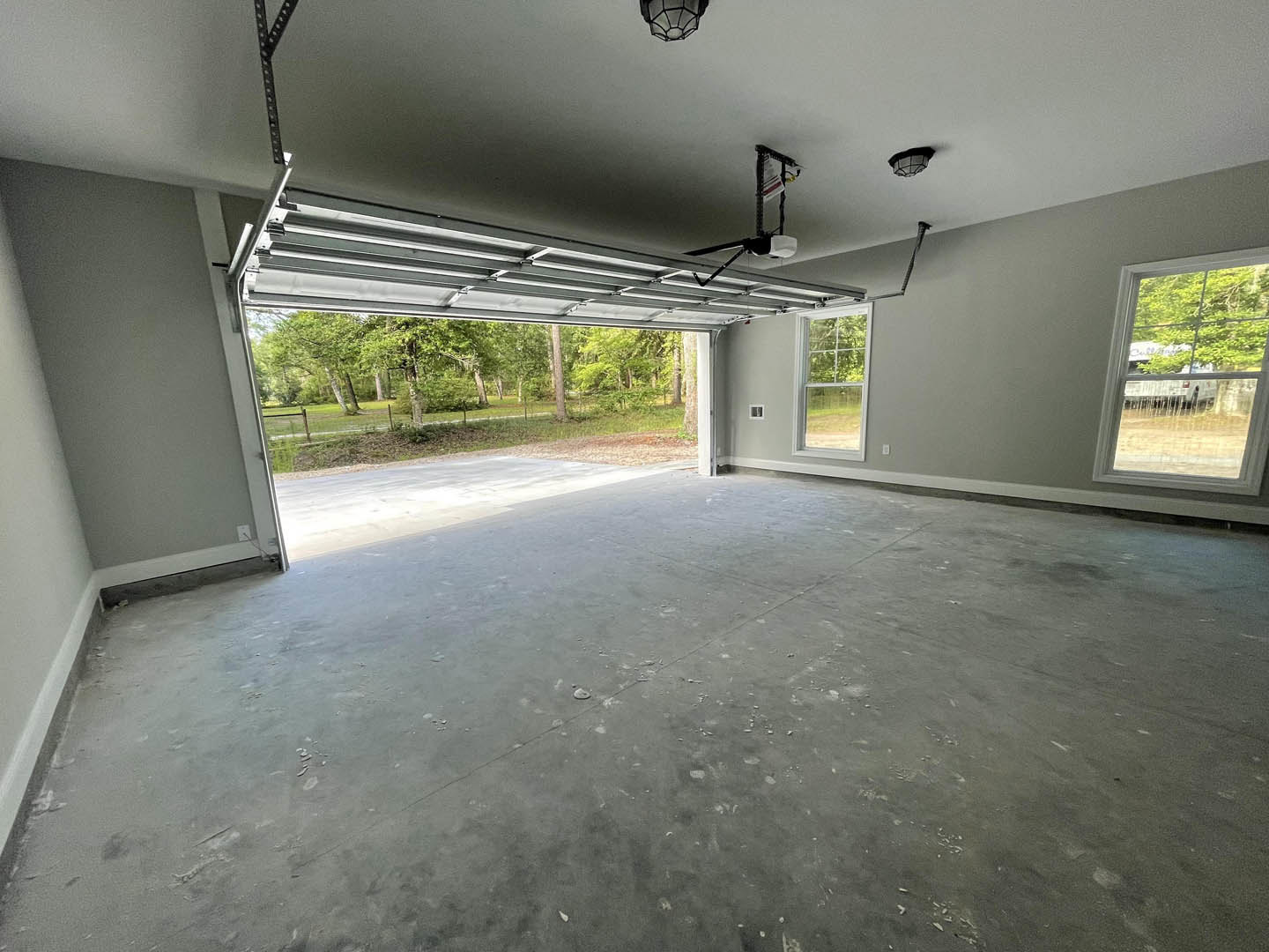 Garage interior with concrete floor, large window overlooking green trees and grass, white van parked outside, white and red sign on black pole near window, ceiling with daylight