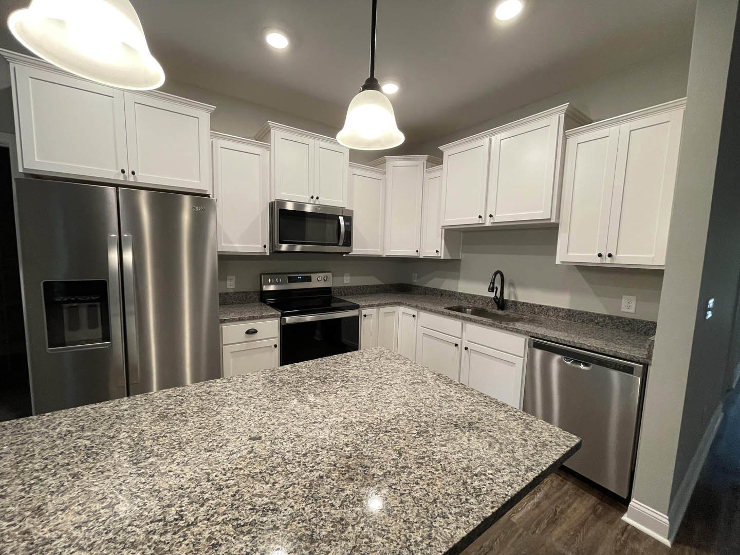 Granite countertops, stainless steel appliances including refrigerator with glass door, built-in microwave, stove, white cabinetry with black handles, tile backsplash, and