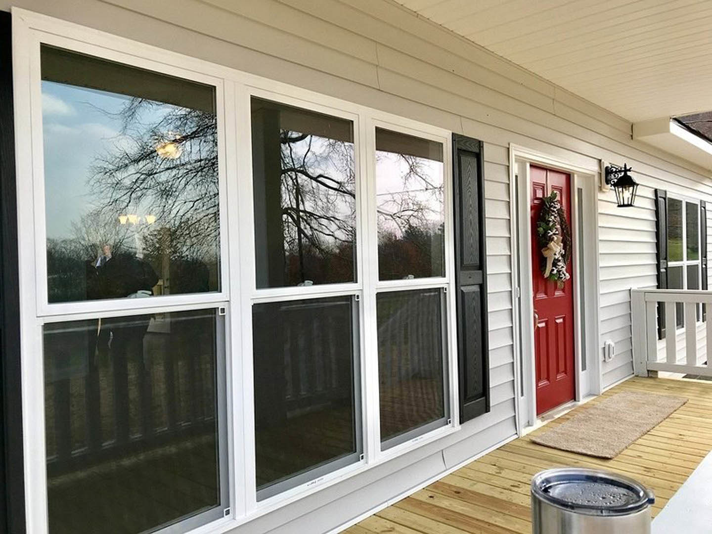 Red front door with a holiday wreath, white siding, porch with wood floor, and white railing