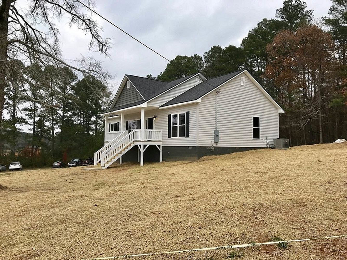 White-painted porch and staircase leading to entry, white-framed windows, fenced yard, mature trees in background, cloudy sky overhead.