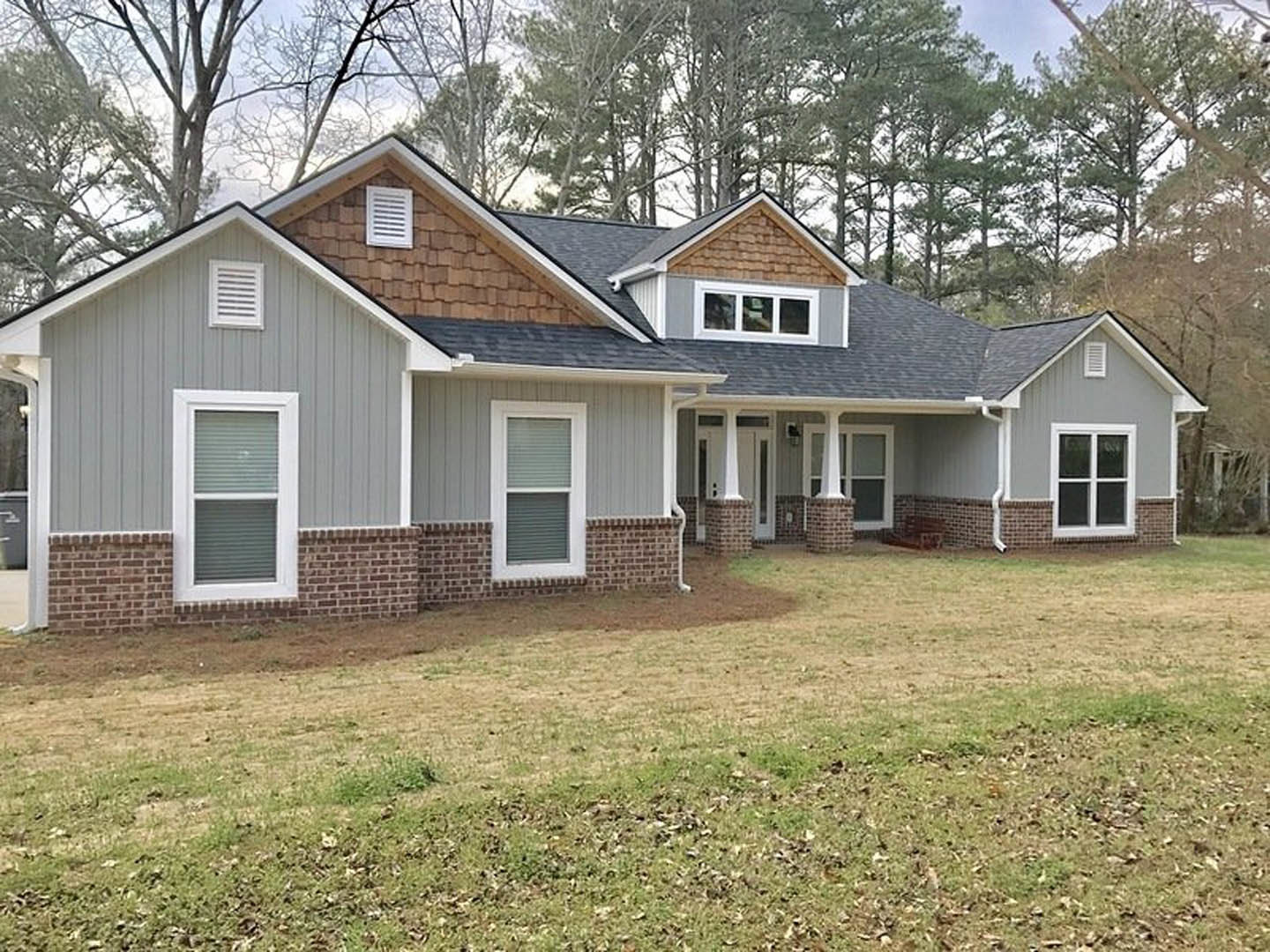 Two-story house with brick and white siding, white-framed windows, front porch, green lawn, and mature trees in the background