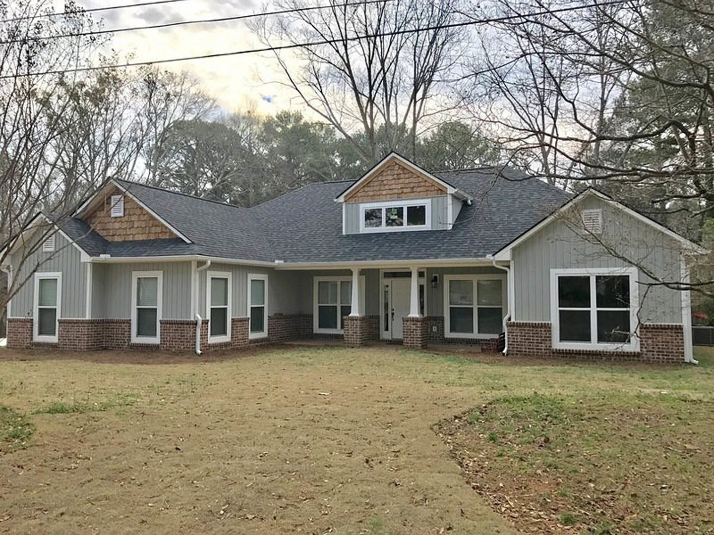 Two-story house with white-framed windows, covered front porch, green lawn, and mature trees in the background