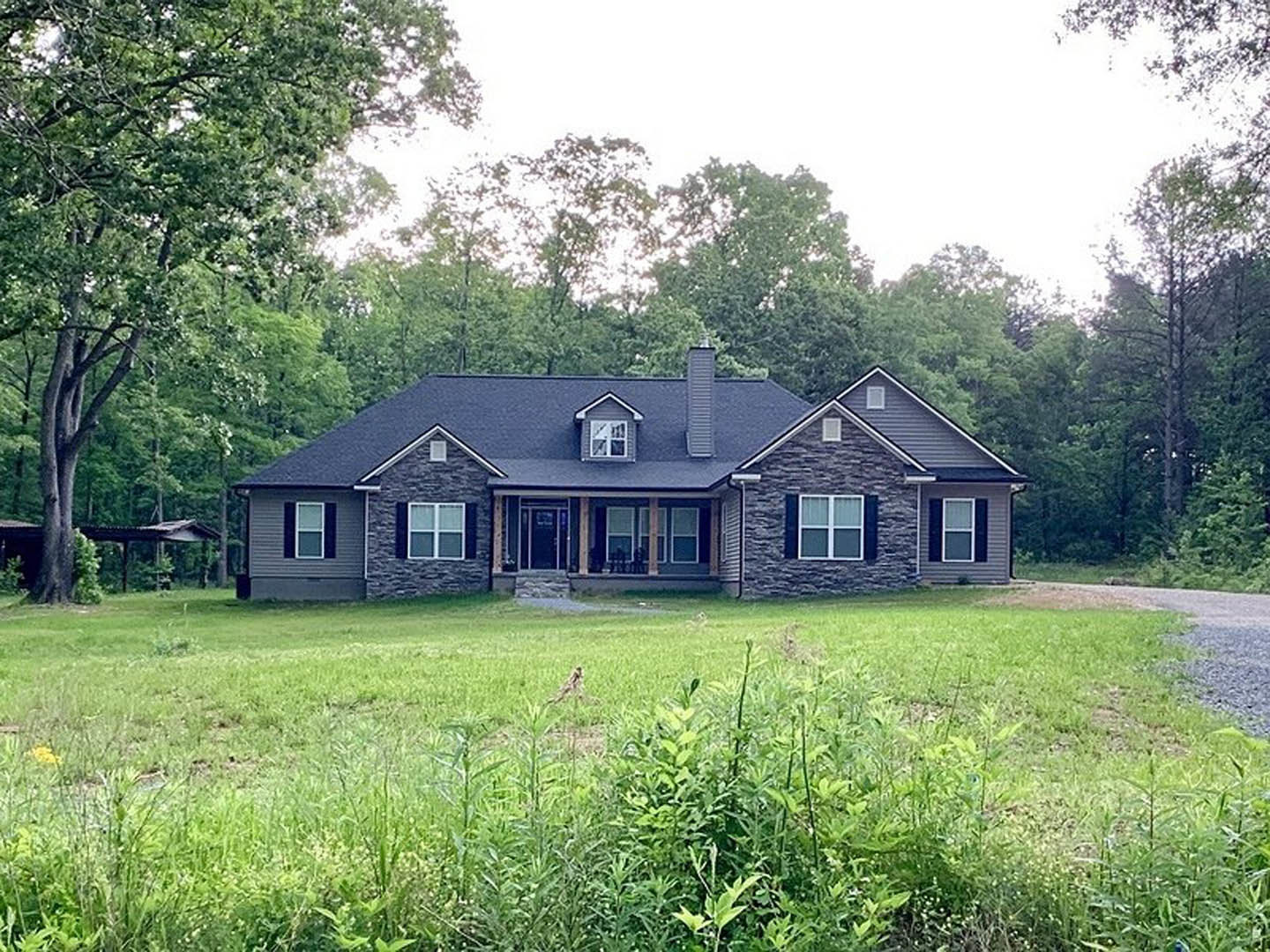 Two-story farmhouse with white siding, covered front porch, large windows, green lawn, mature trees, and blue sky in background
