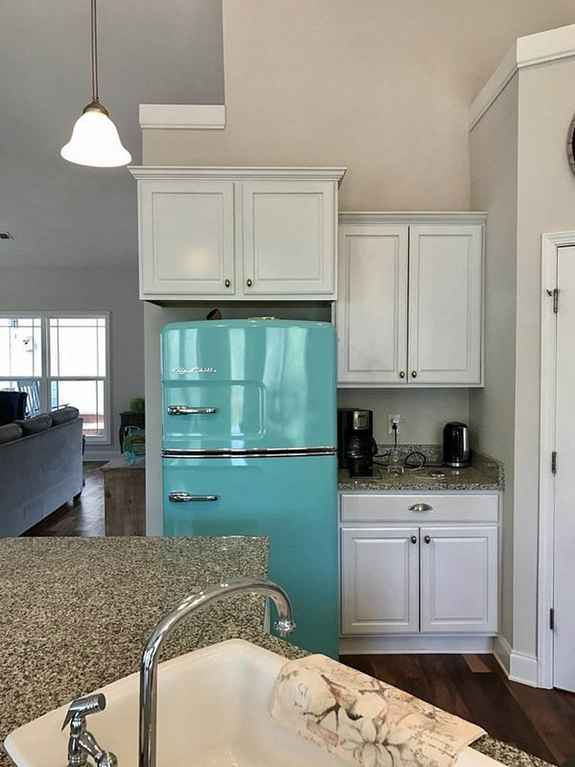 Blue refrigerator with stainless handles beside white cabinetry, marble countertop, and undermount sink with chrome faucet in a modern kitchen.