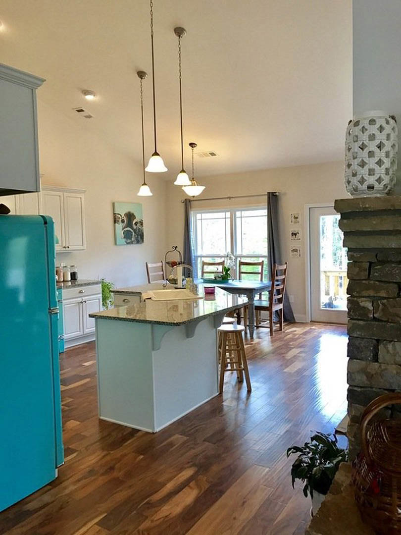 Blue refrigerator beside white cabinetry, wood dining table with chairs, light stone countertop on kitchen island, hardwood flooring, modern ceiling, metal stool.